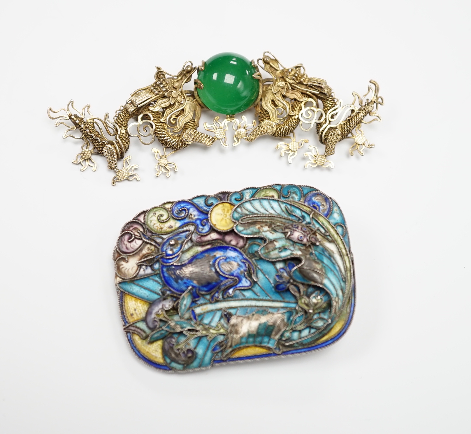 A Chinese? white metal and polychrome enamelled brooch, depicting a hare amongst foliage, 59mm(a.f.), together with a similar gilt white metal filigree and cabochon green paste set brooch.